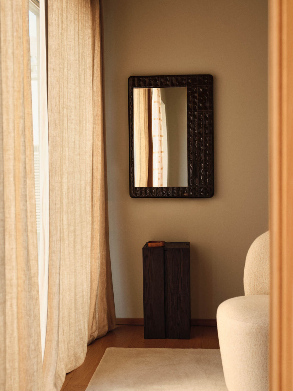Pedestal in dark stained oak in a sunlit corner below a textured wall mirror