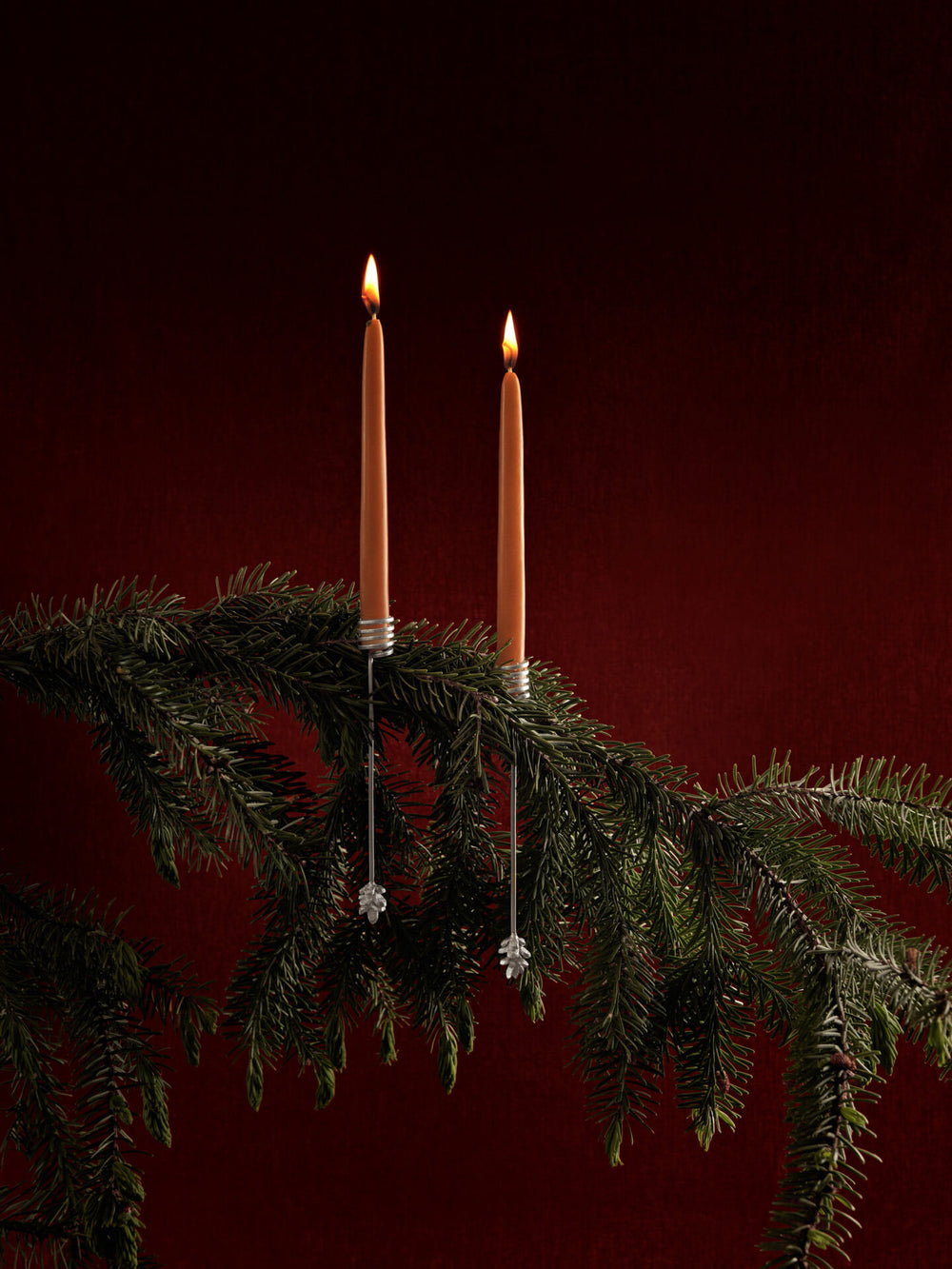 Two holders clipped to a fir branch with lit candles, cone pendants hanging below
