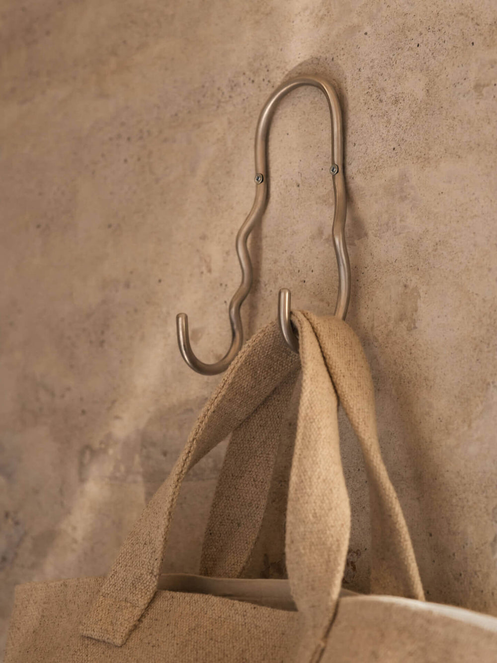 Wavy double hook wall mounted, holding the straps of a woven tote bag