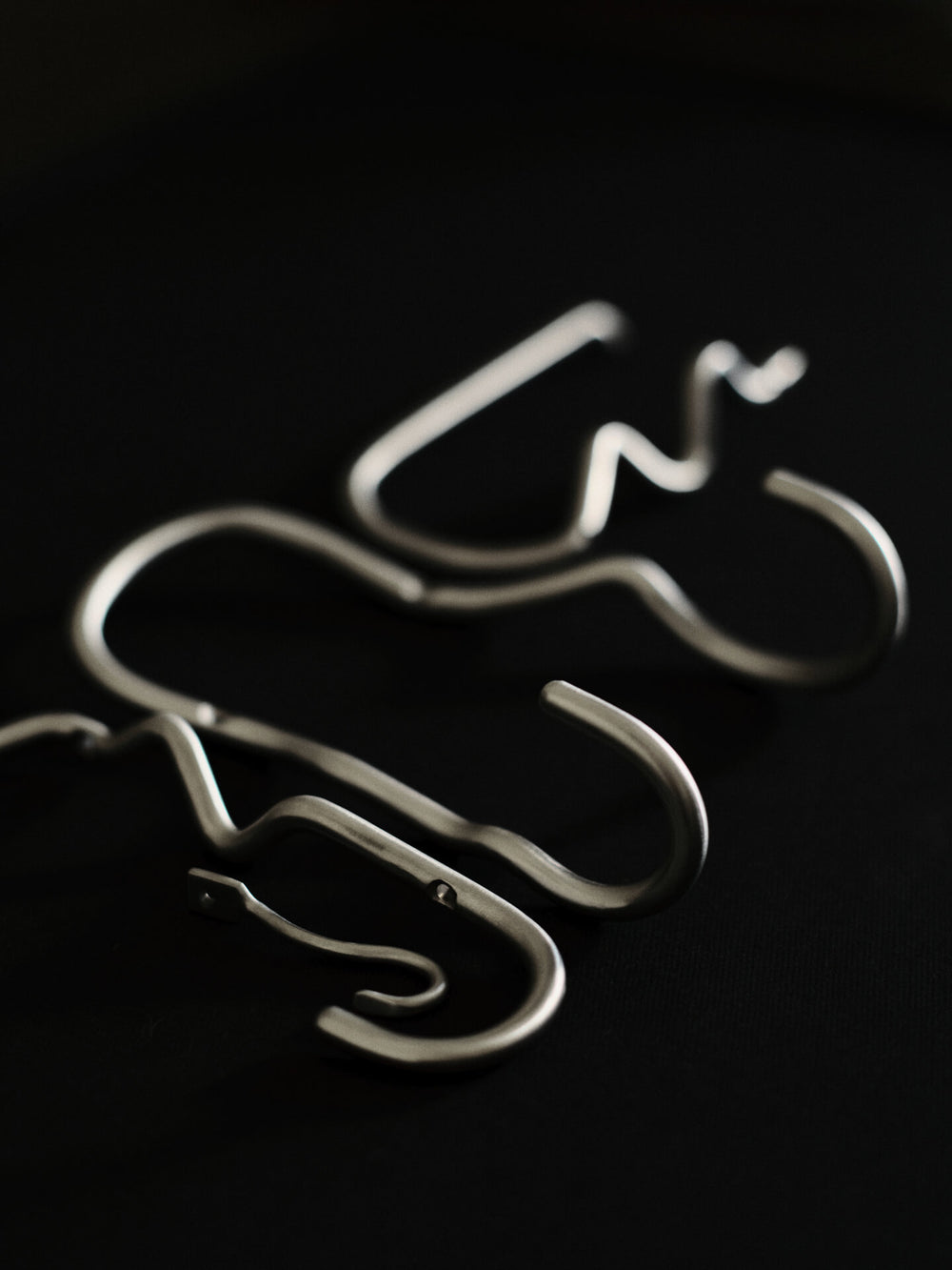 Two curved double hooks lying on a black surface, close-up of the bent wire forms