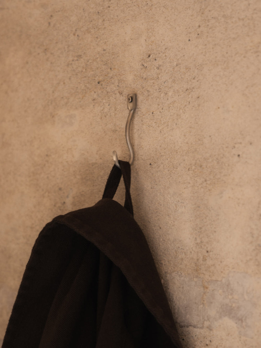 Curved wall hook mounted on a pale wall with a dark brown towel hanging from it