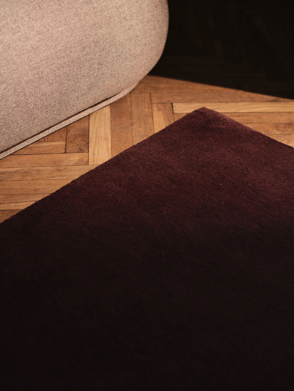Corner of the dark pecan rug on herringbone flooring beside a beige upholstered seat