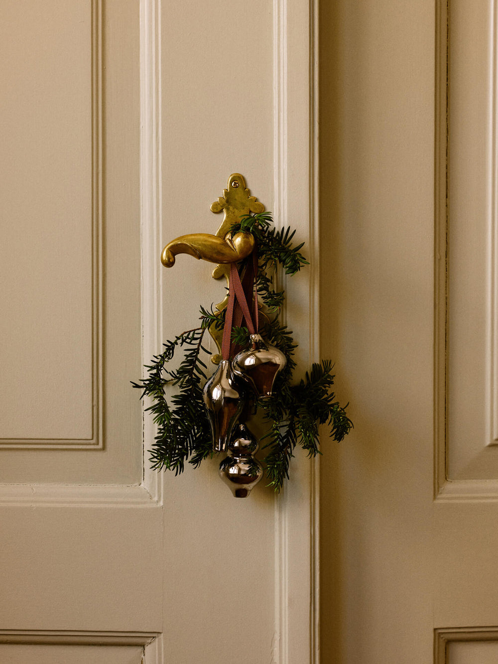 Three ornaments on ribbons hung with fir sprigs from a door handle on a panelled door