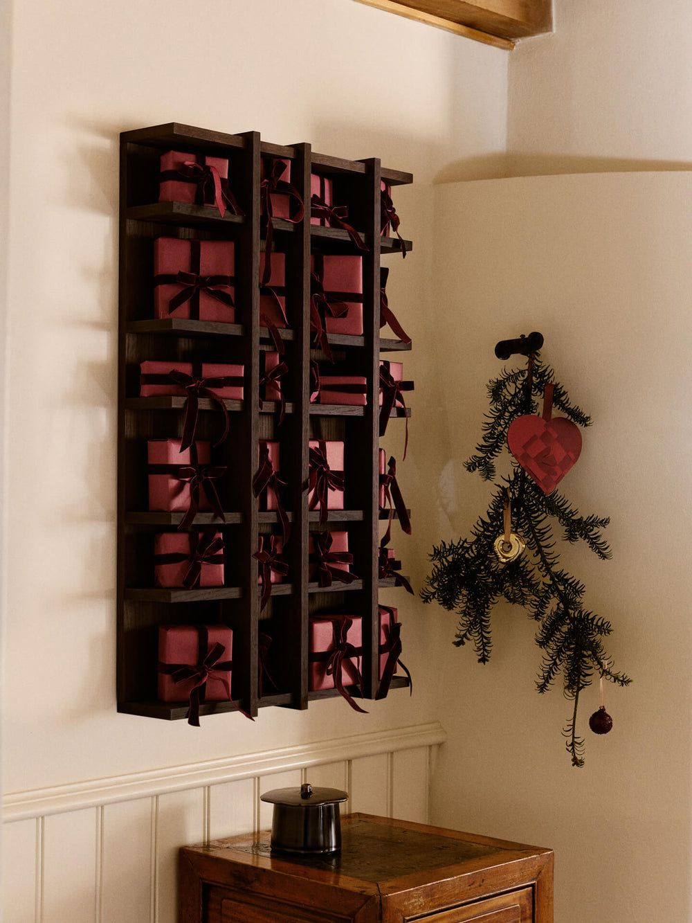 Hallway with the ornament hanging from a branch on the wall, beside a dark shelf of red wrapped gifts