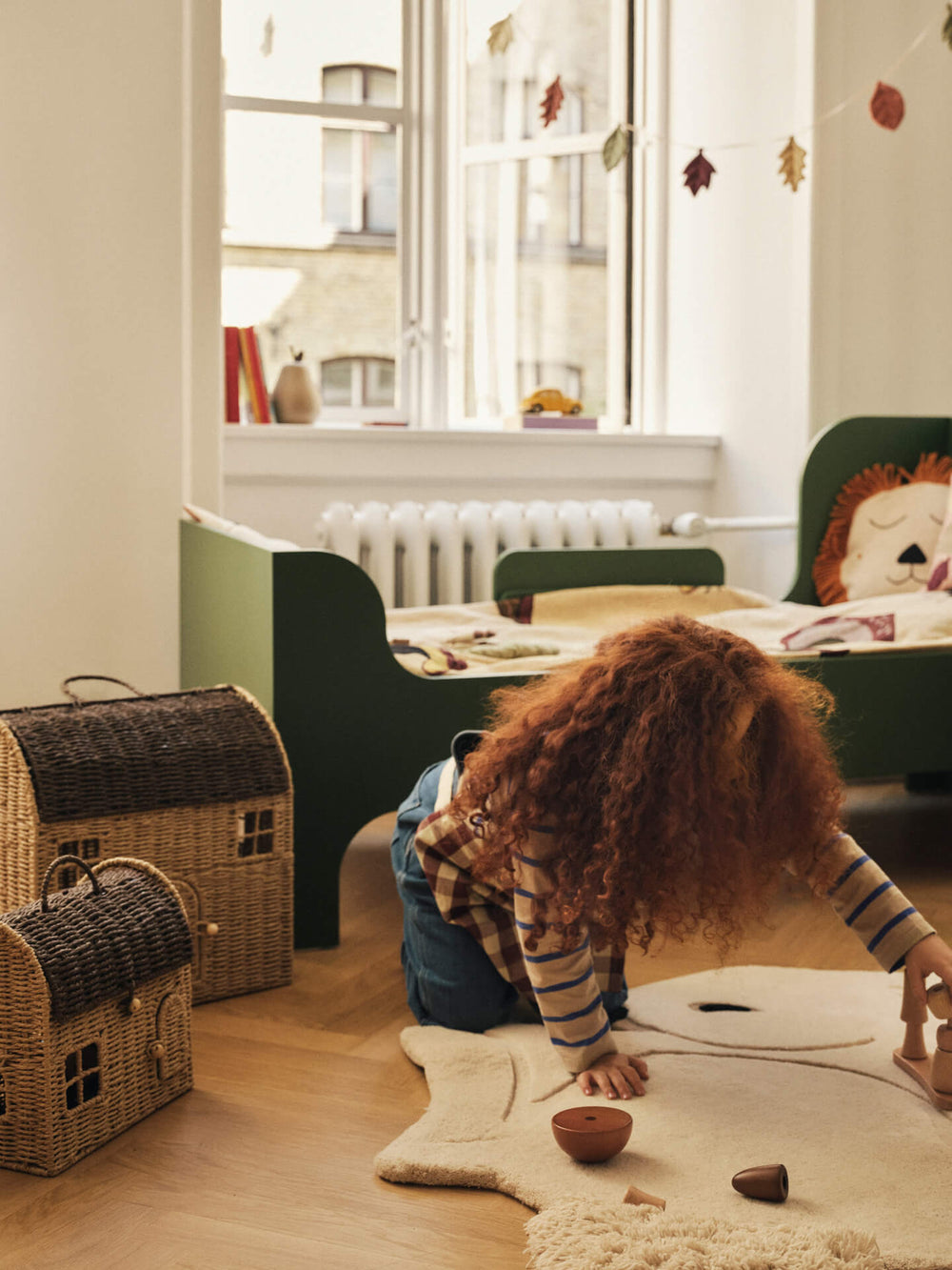Child's room with the two house-shaped storage baskets on the floor beside a green bed and star rug