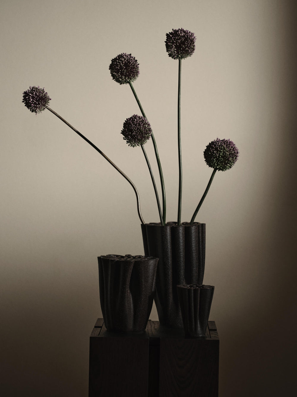 Three vases in dark brown grouped on dark plinths, tall one holding purple allium stems