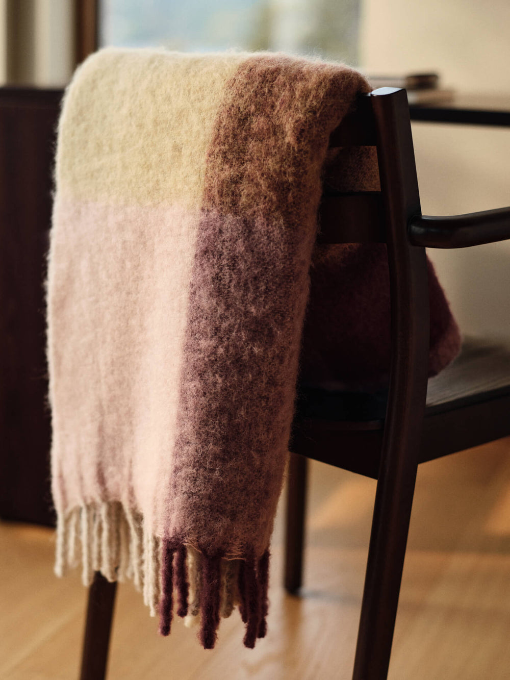 Fringed blanket in butter and pale rose draped over a dark chair back in a dining room