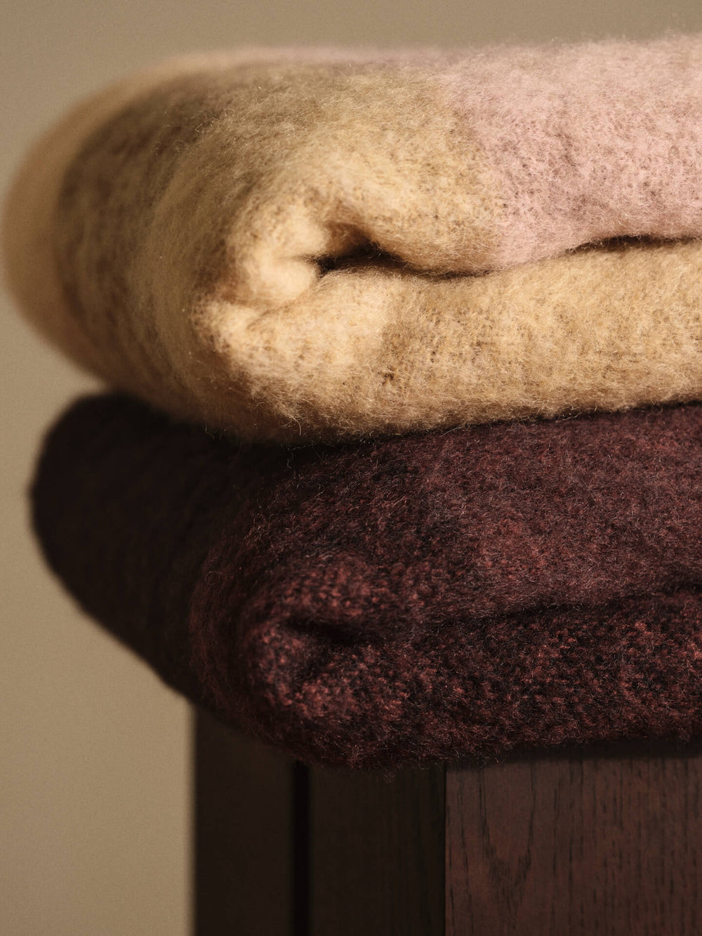 Close-up of the folded blanket in butter and pale rose stacked on a dark red one