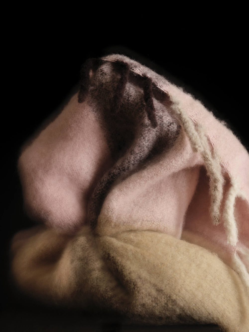 Close-up of the blanket's brushed surface and knotted fringe, pale rose bleeding into butter