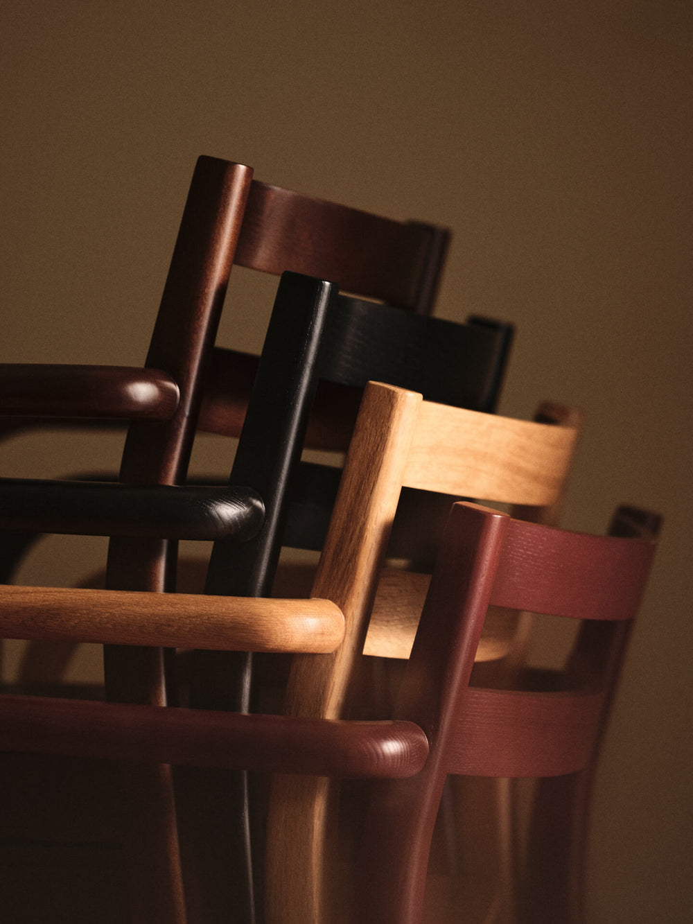 Four stacked dining chairs with arms in brown, black, natural and dark red