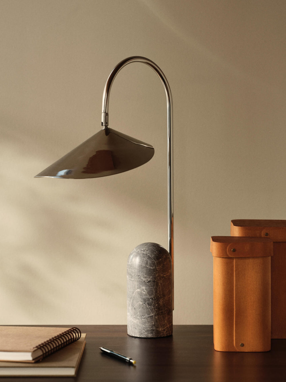 The table lamp on a dark desk with a notebook, pen and two tan storage boxes