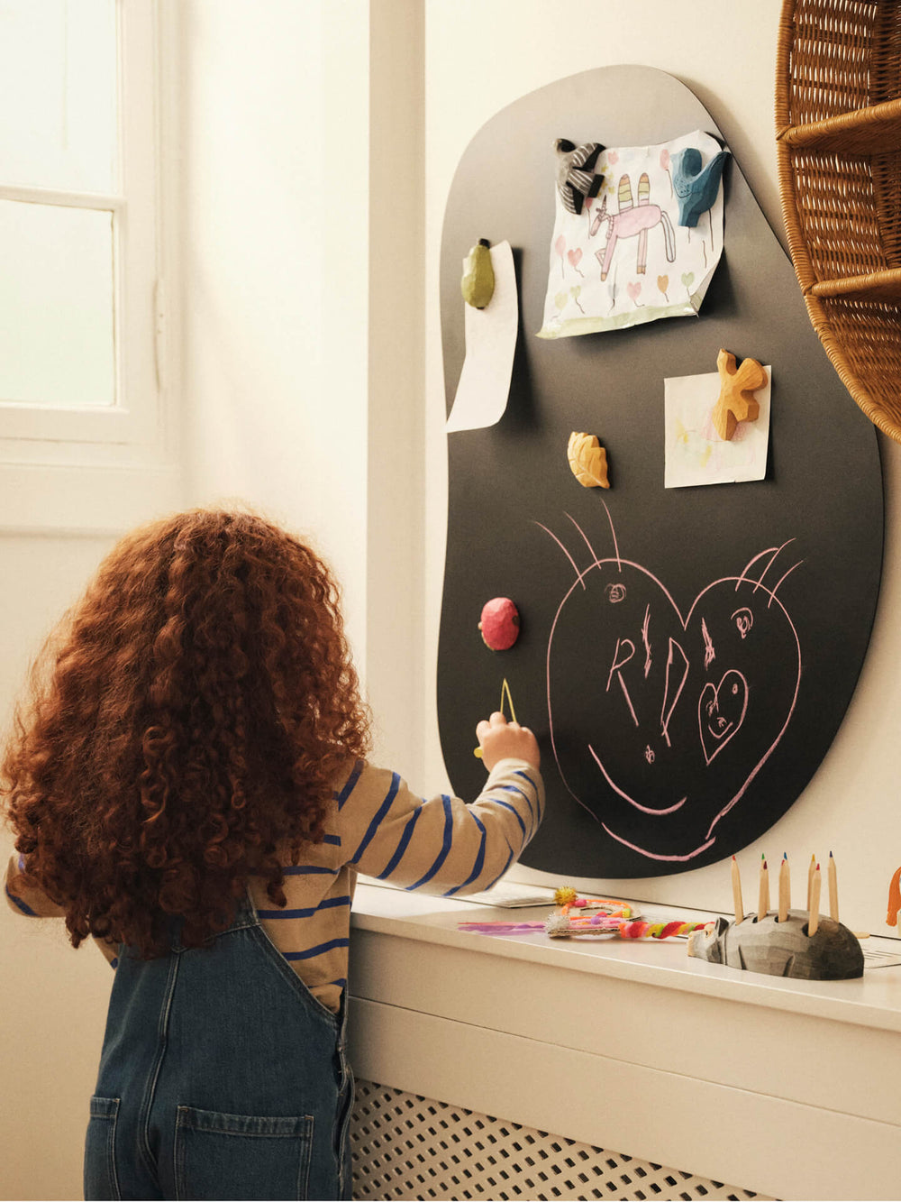 Child drawing on a black magnetic wall board where the hand-carved magnets hold up drawings