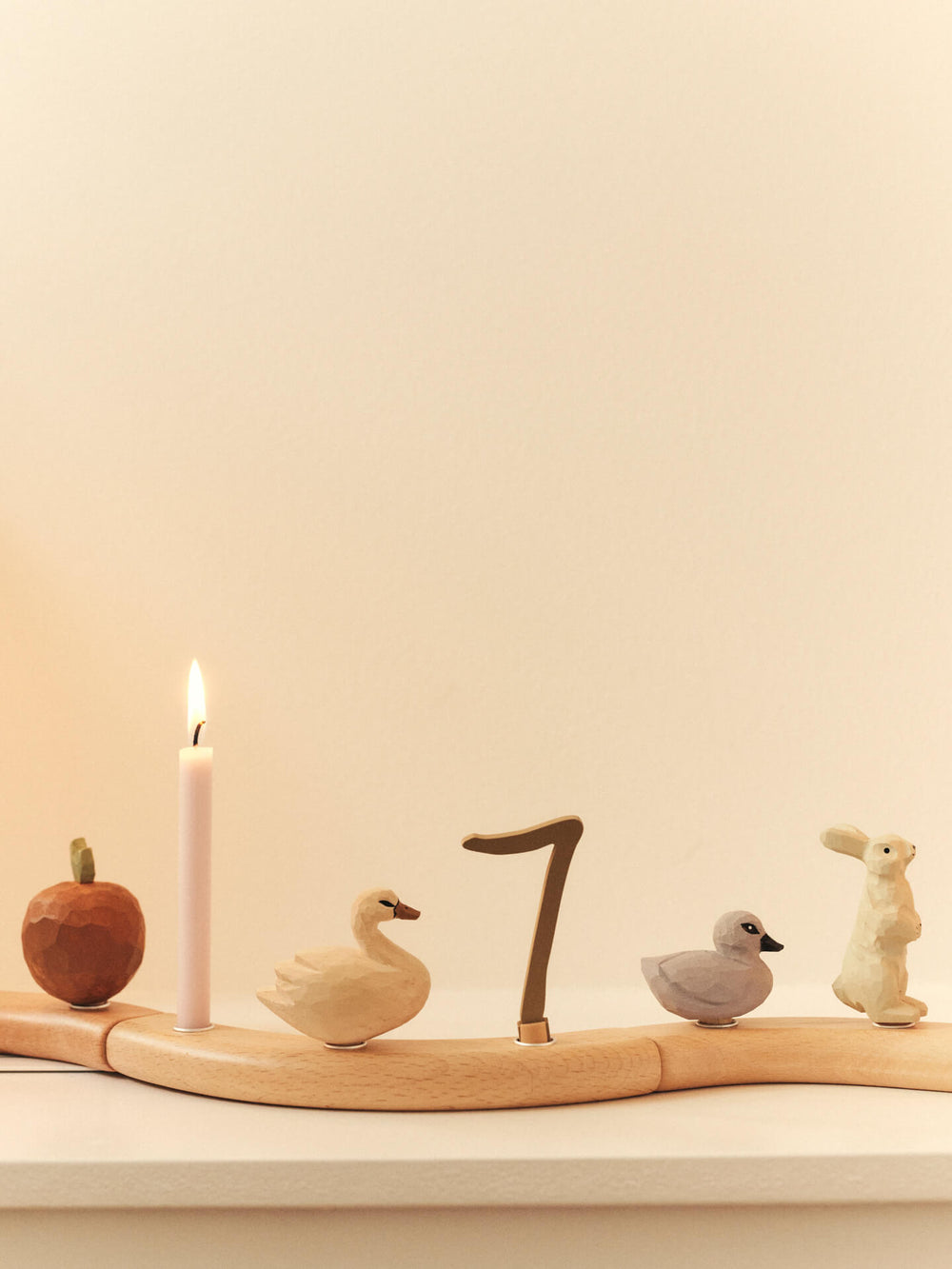 Swan and duckling figurines on a curved celebration ring with a lit candle, apple, number 7 and rabbit