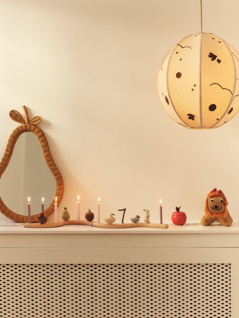 Swan and duckling figurines on a curved candle holder with lit candles, below a round pendant lamp and pear-shaped mirror
