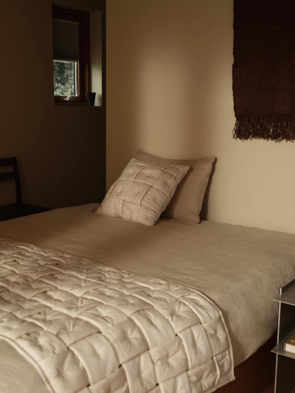 Bedroom with the fringed wall rug in dark chocolate hung above a bed with quilted beige bedding