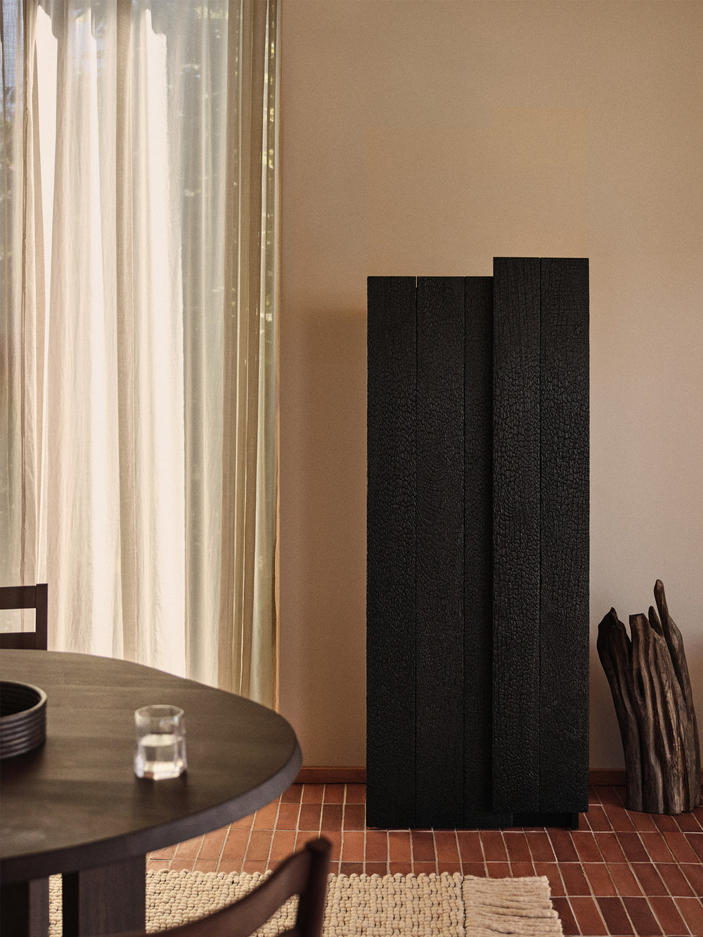 Tall black cabinet with charred offset doors in a dining room with round table and tiled floor