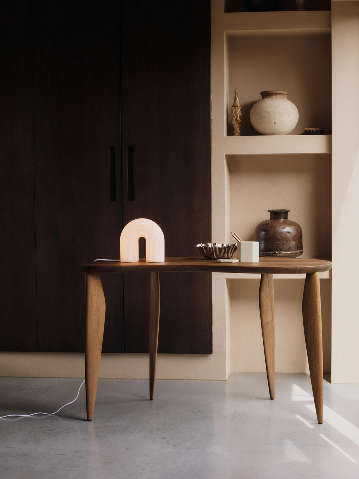 Lit arched table lamp on a slim console table, with a ribbed bowl and vases in wall niches