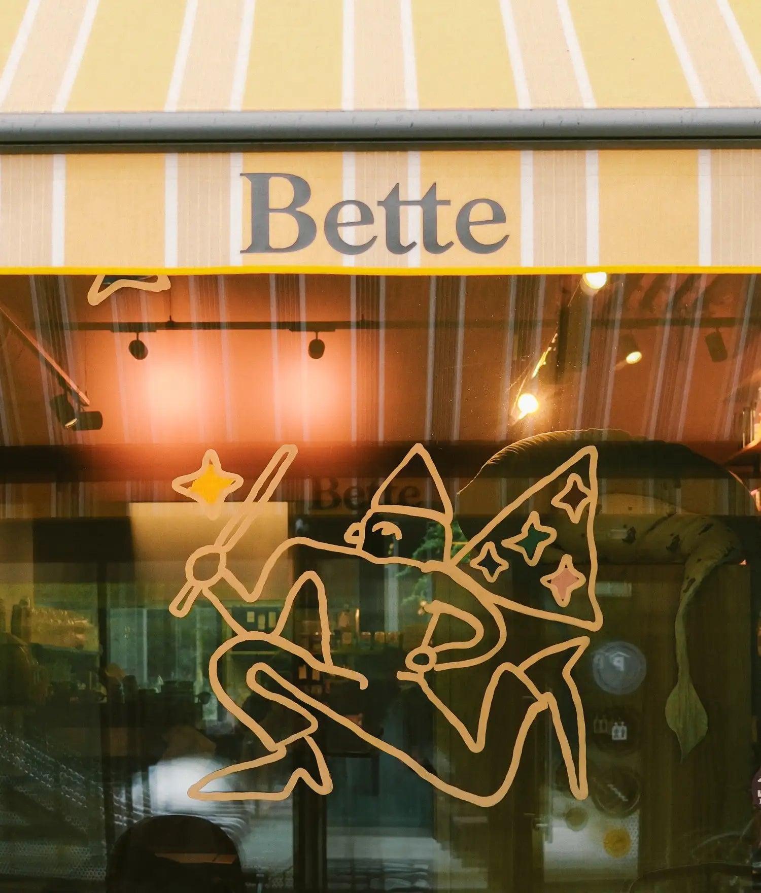 Shop window with a striped awning reading Bette, fairy drawn in outline on the glass